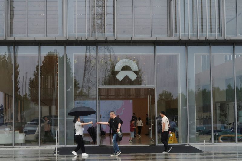 © Reuters. FILE PHOTO: A staff member hands an umbrella to a man outside a store of Chinese electric vehicle (EV) maker Nio at the company's manufacturing base in Hefei, Anhui province, China June 28, 2024. REUTERS/Ellen Zhang/File Photo